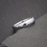 Thin silver ring with multi-faceted polished tungsten face photographed on a slate background