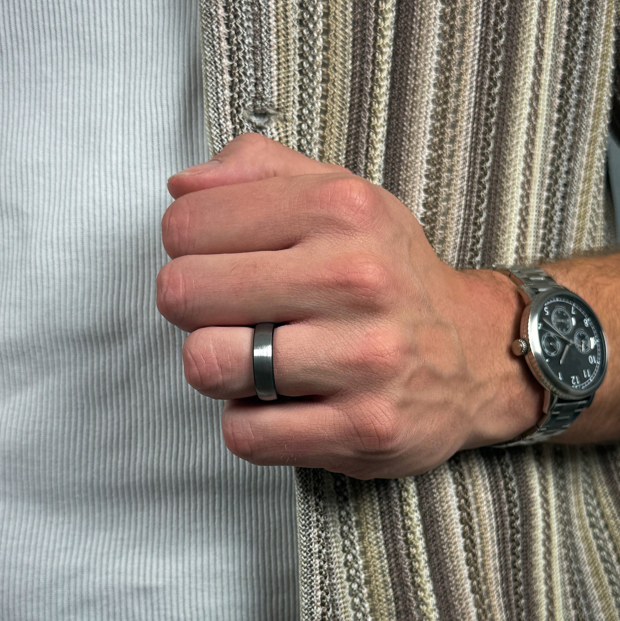 Hand wearing a silver ring and wristwatch on a striped fabric background