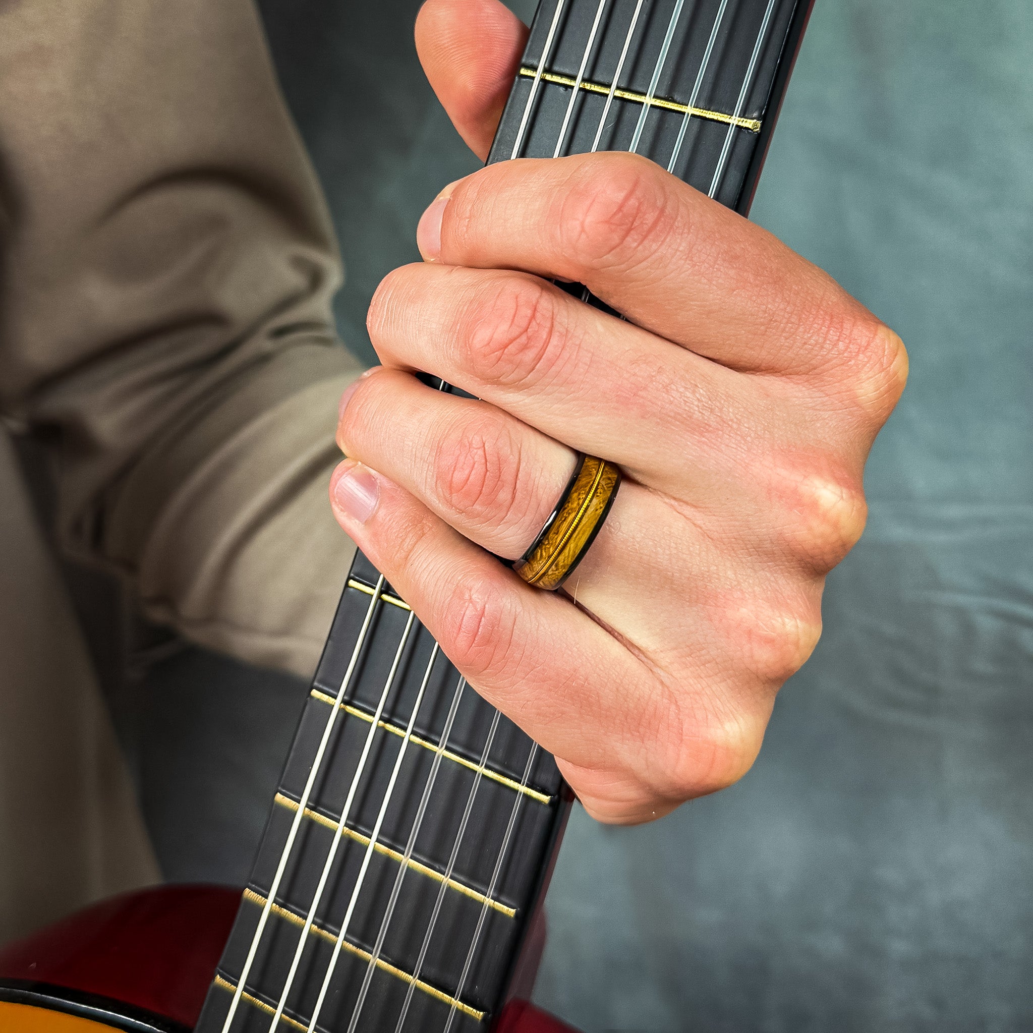 man wearing a black guitar string wedding band holding a guitar