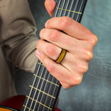 man wearing a black guitar string wedding band holding a guitar
