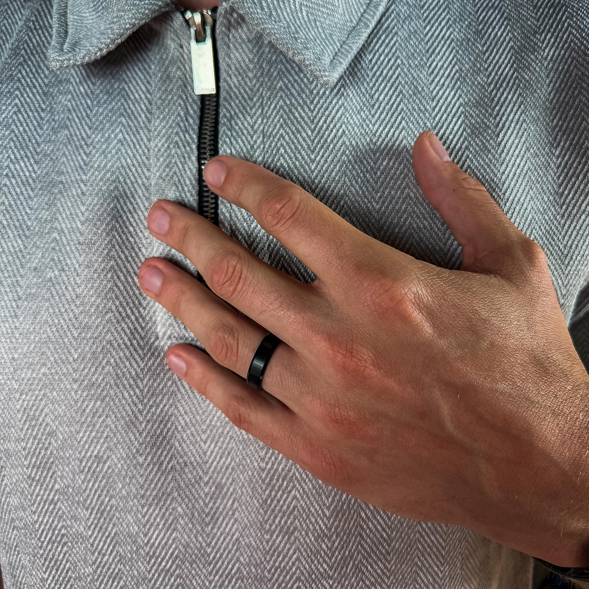Hand with a black ring on a gray textured fabric background