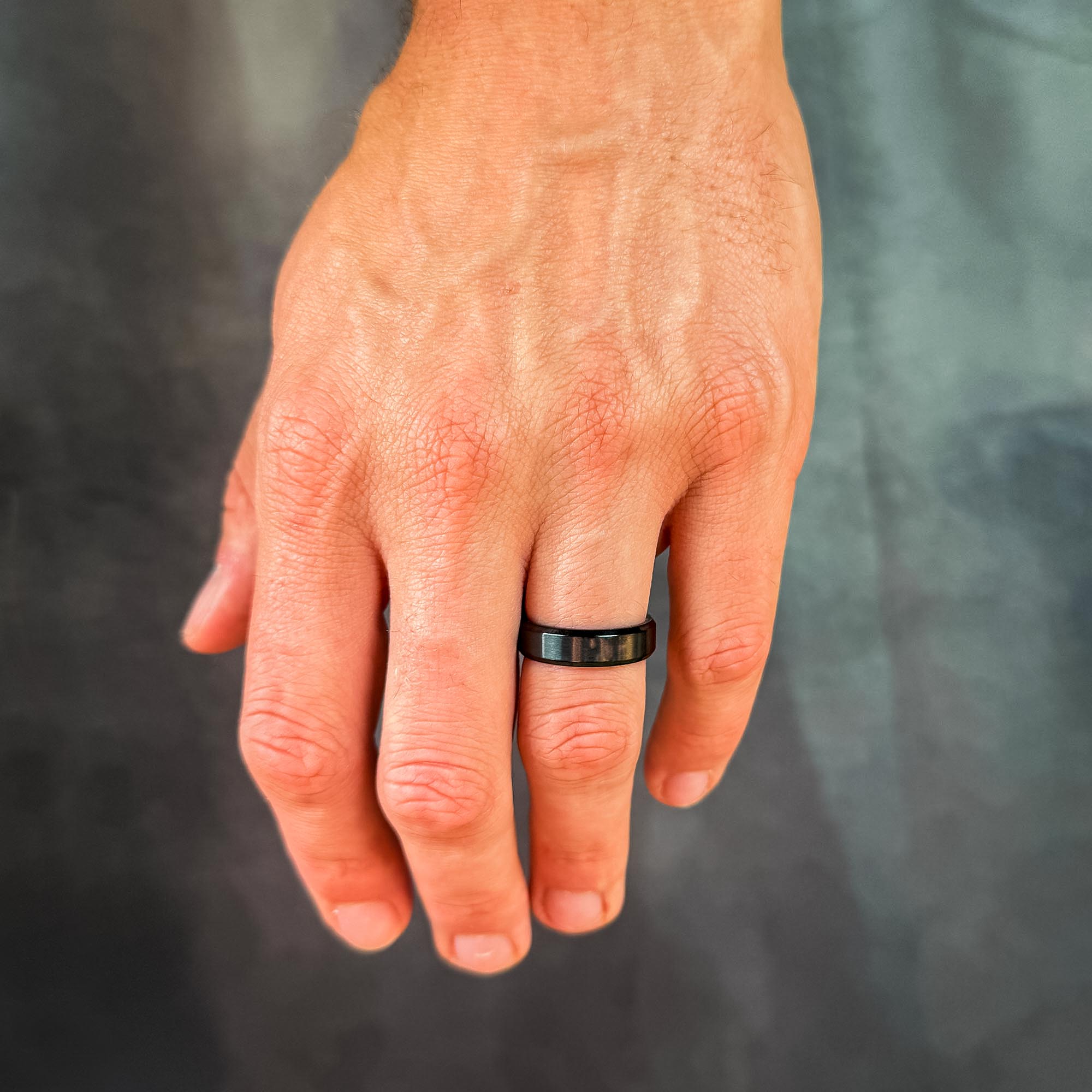 Hand wearing a black ring on a dark background