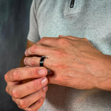 Close-up of a person wearing a black ring on a neutral background