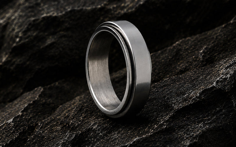 silver tungsten anxiety fidget ring with spinning gears photographed on a neutral coloured material