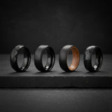 a collection of mens black wedding bands photographed on a dark stone surface