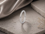 Slim 2mm silver tungsten wedding ring standing on soft neutral stone with elegant feminine luxury styling and warm cinematic lighting.