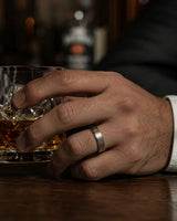 Man wearing an 6mm brushed silver tungsten wedding ring with polished edges and genuine maple wood sleeve while holding a crystal whiskey glass.