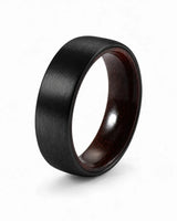Brushed black tungsten wedding ring with a maple wood sleeve interior shown at an angled view on a white background.