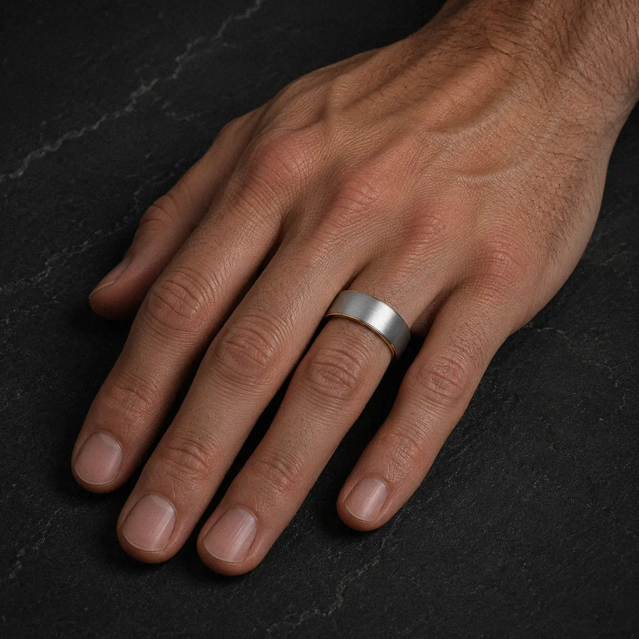 Man wearing a brushed silver tungsten wedding ring with polished gold interior on his left ring finger.