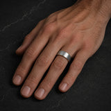 Man wearing a brushed silver tungsten wedding ring with polished gold interior on his left ring finger.