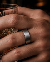 Close up of a man wearing a brushed silver tungsten wedding ring with a maple wood sleeve interior while holding a whiskey glass.