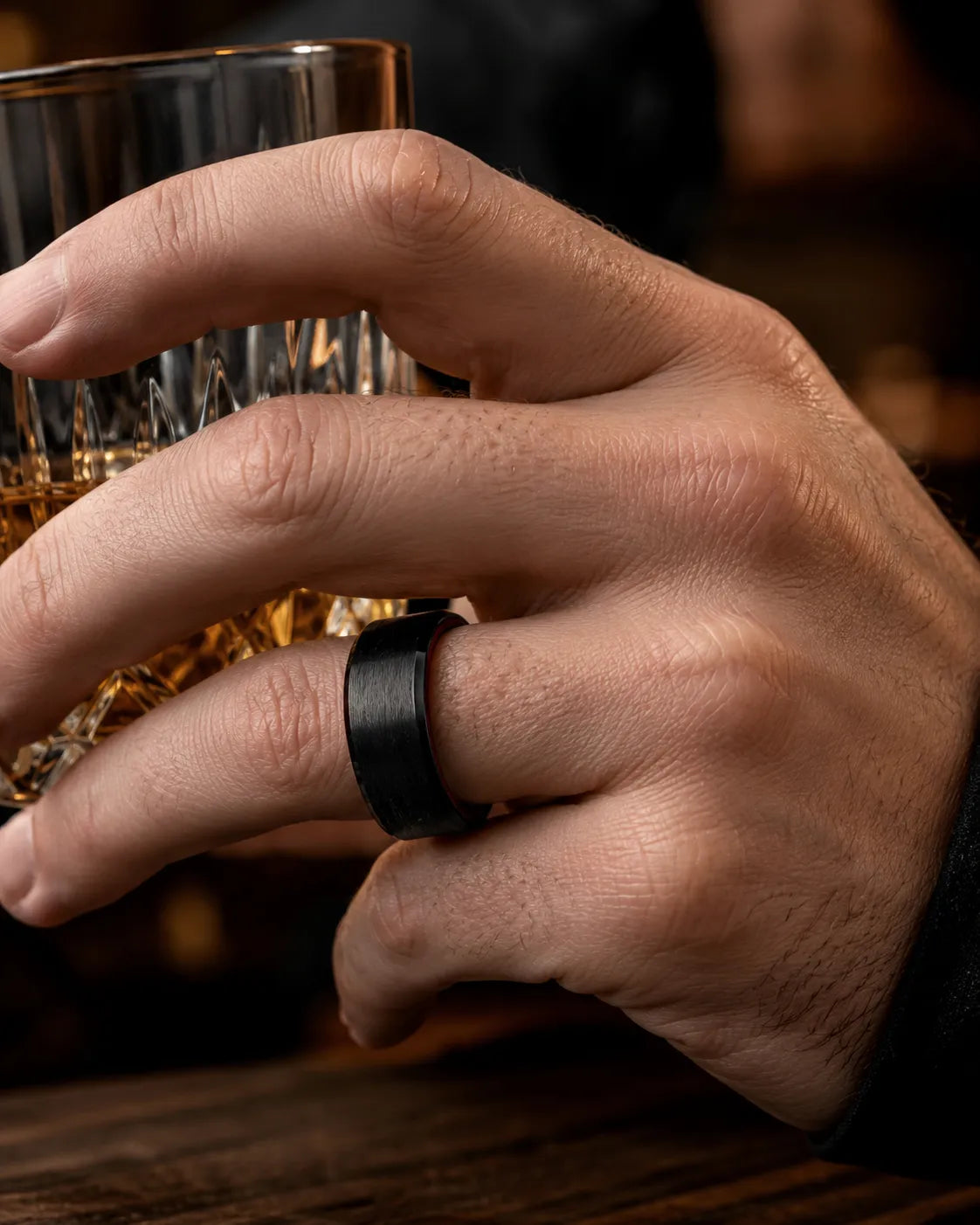 Macro close up of an 8mm brushed black tungsten wedding ring with polished edges and maple wood sleeve on a man's hand