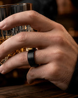 Macro close up of an 8mm brushed black tungsten wedding ring with polished edges and maple wood sleeve on a man's hand