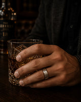 Man wearing an 8mm brushed silver tungsten wedding ring with polished edges and maple wood sleeve while holding a whiskey glass