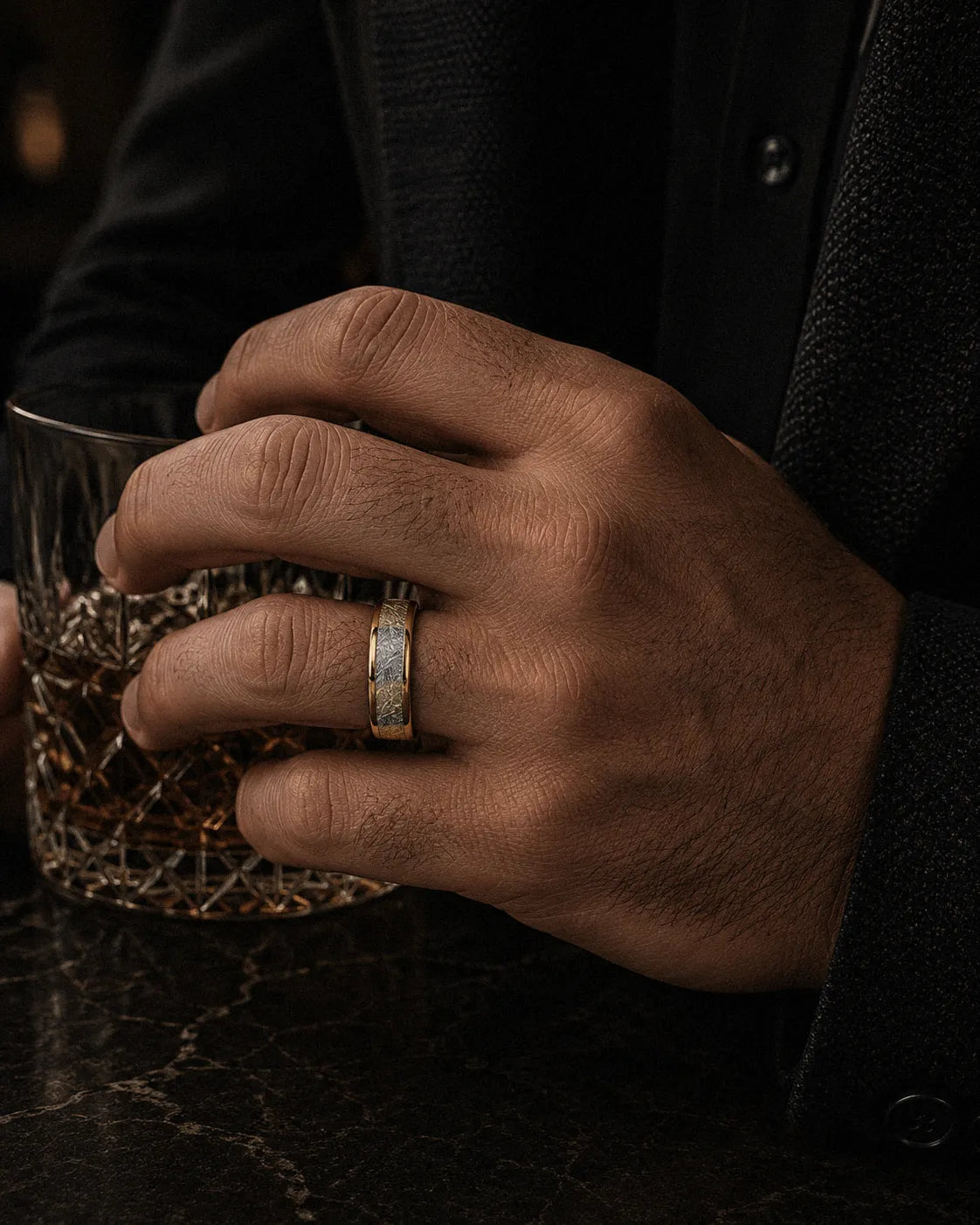 8mm gold meteorite inlay tungsten wedding ring worn by a man holding a crystal whiskey glass
