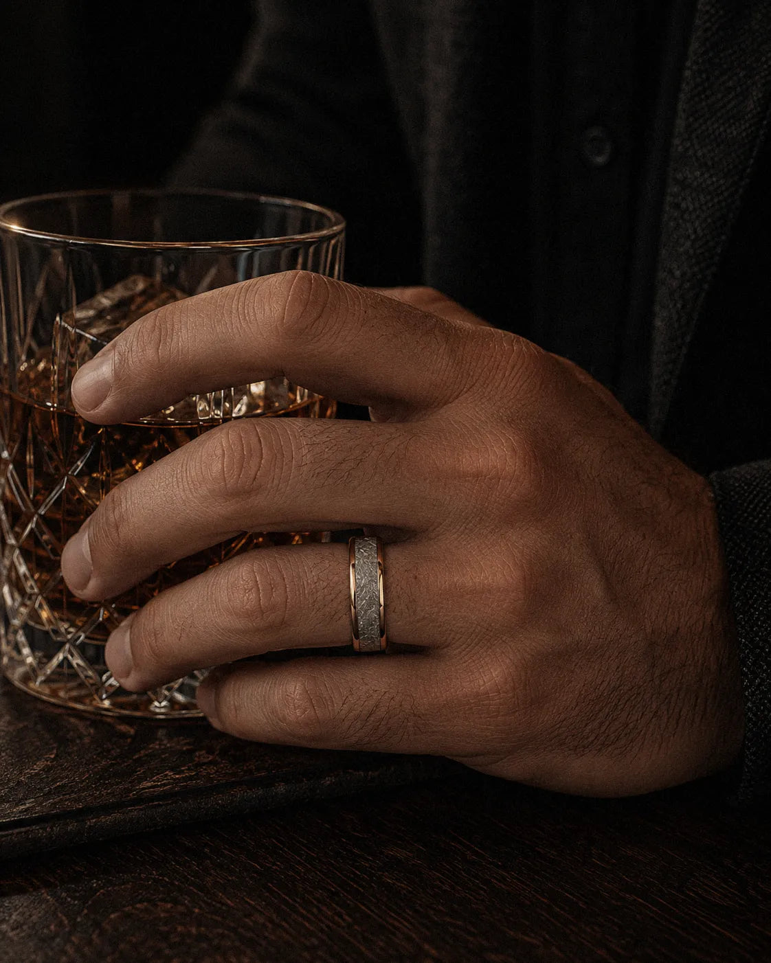 8mm rose gold meteorite inlay tungsten wedding ring worn by a man holding a crystal whiskey glass