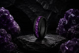 Luxury amethyst wedding ring collection hero image featuring a black tungsten ring with deep purple crushed amethyst inlay on a dark cinematic stone background.