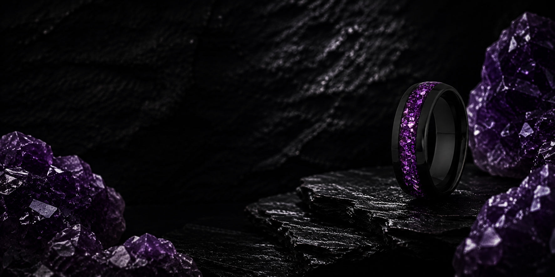 Wide desktop banner for amethyst wedding rings collection featuring a black tungsten ring with purple gemstone inlay positioned on a dark luxury slate background.