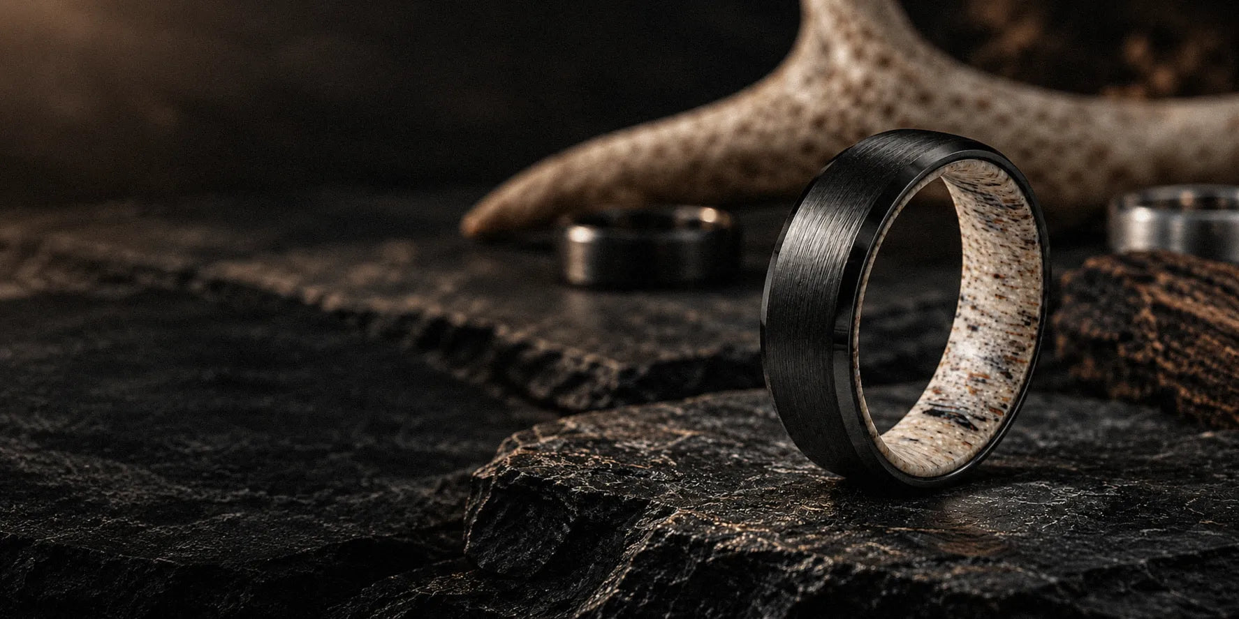 Black tungsten antler wedding ring displayed on dark slate with natural deer antler