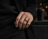 Man wearing a black tungsten wedding ring with blue inner band in a dark luxury lifestyle setting.