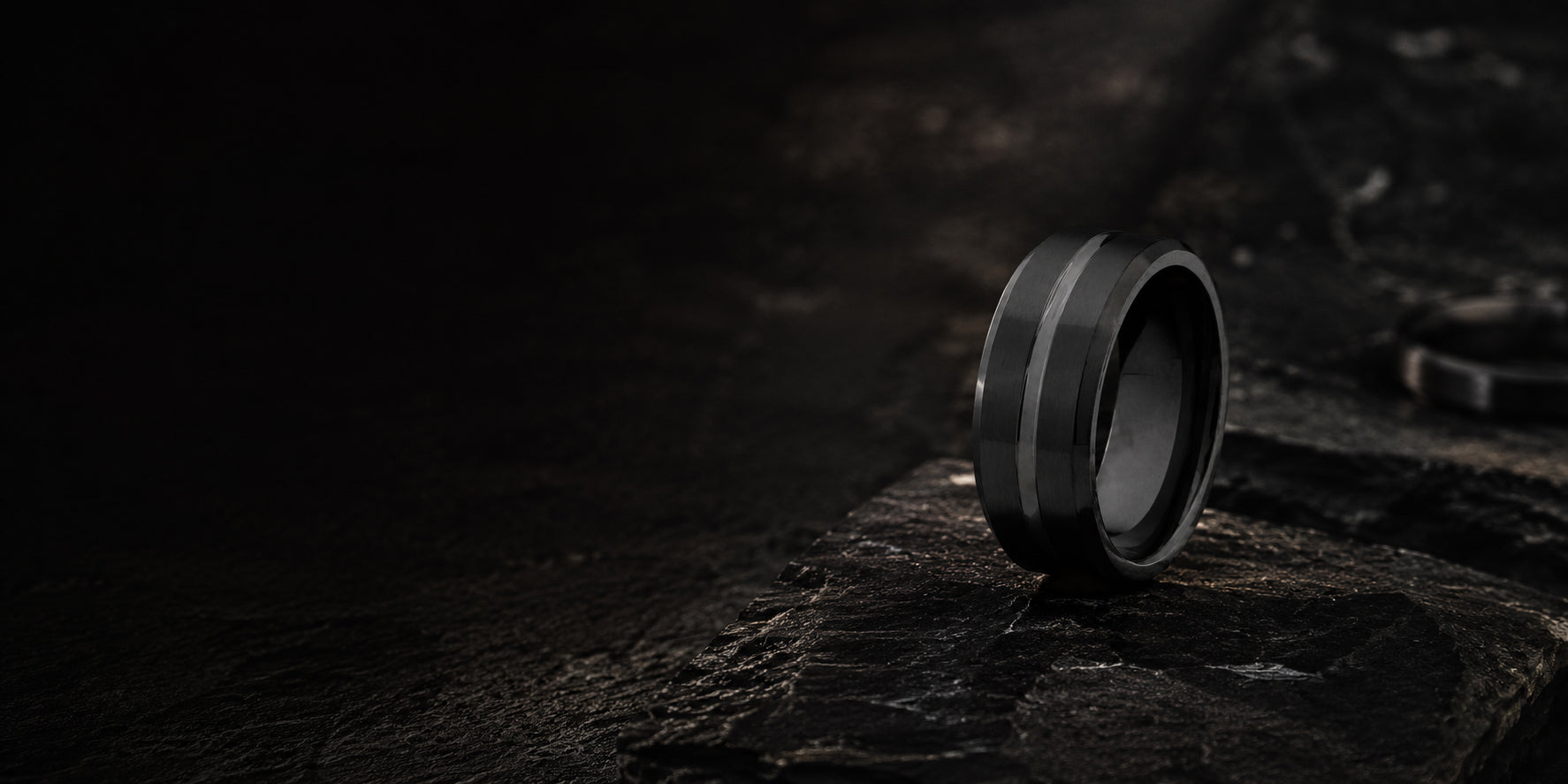 Luxury black tungsten wedding ring desktop hero banner with dark charcoal stone textures and cinematic masculine ecommerce styling.