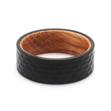 Top view of a black hammered tungsten wedding ring with a real oak whiskey barrel wood interior.