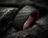 Extreme macro close-up of a black hammered men’s wedding ring with wood interior showing detailed texture and rugged craftsmanship on dark slate stone.