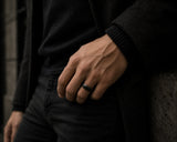 Man wearing a black brushed wedding ring with polished edges in a dark luxury lifestyle setting with cinematic lighting.