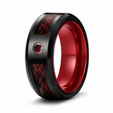 Black tungsten wedding ring with red Celtic dragon inlay, red gemstone and polished red comfort fit interior shown at an angled studio view on a white background.