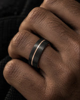 Close-up of a brushed black men’s wedding ring with a rose gold offset groove worn on the ring finger.