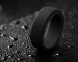 Ultra close-up macro photograph of a black silicone men’s wedding ring with matte texture and dark rugged background