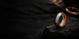 Luxury black and silver tungsten wedding ring with rose gold interior positioned on dark slate background with cinematic lighting and negative space for website banner text.