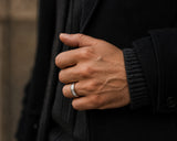 Man wearing a black and silver brushed wedding ring with rose gold interior in a dark luxury lifestyle setting with premium masculine styling.