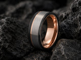 Ultra detailed macro photograph of a black and silver men’s wedding ring with rose gold interior resting amongst rugged volcanic rock textures.