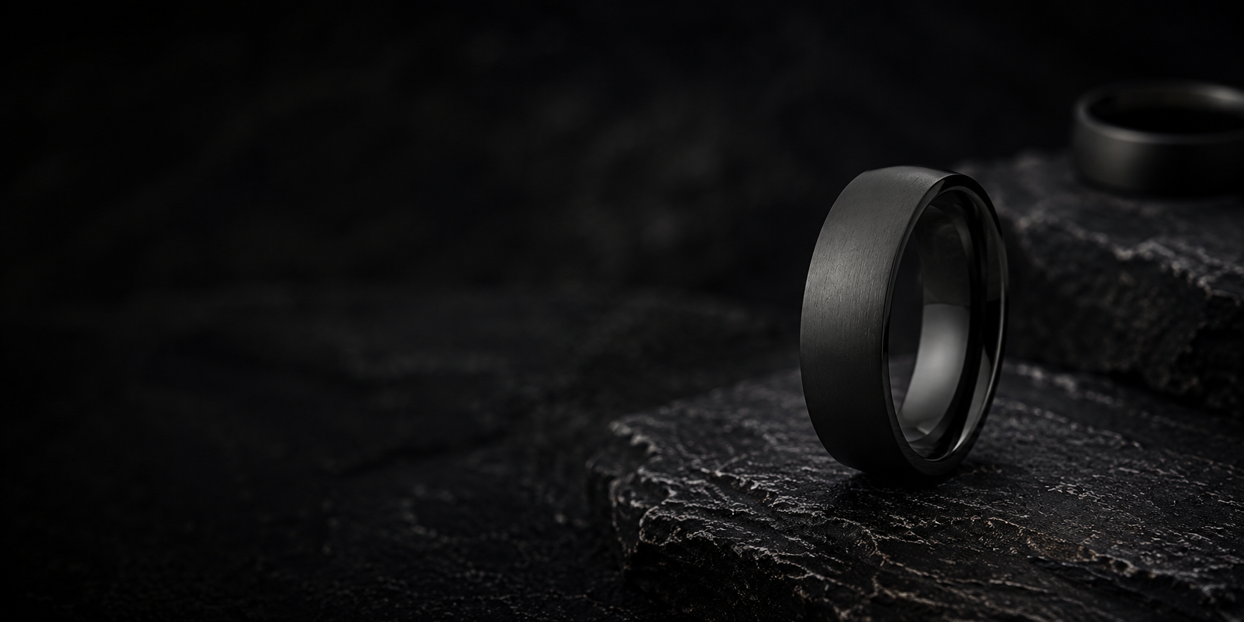 Black titanium men’s wedding ring photographed on dark volcanic rock with moody cinematic lighting and rugged charcoal textures.