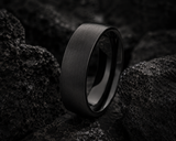 Extreme macro photograph of a black titanium men’s wedding ring resting amongst volcanic rock with detailed brushed texture and polished edges.