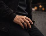 Man wearing a black titanium wedding ring with dark knitwear and modern urban styling in a luxury cinematic lifestyle scene.