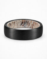 Brushed black tungsten wedding ring lying flat showing natural antler inner sleeve