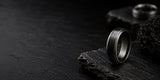 Luxury black men’s wedding ring positioned on rugged charcoal slate with dark moody lighting and premium masculine styling.