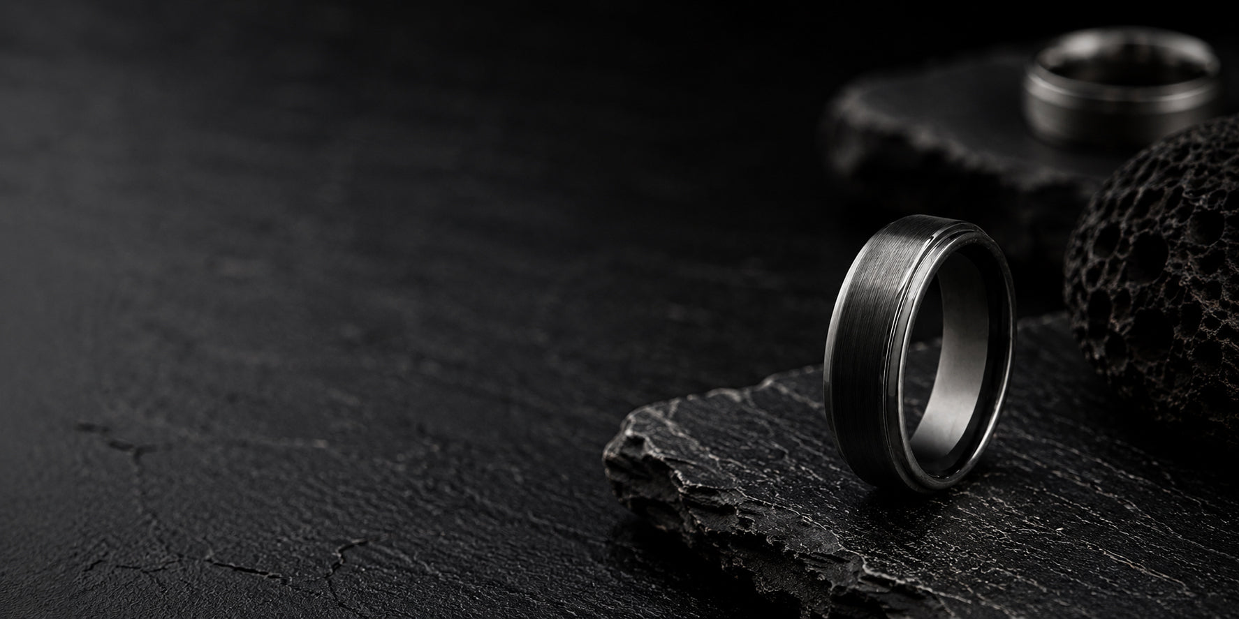 Luxury black men’s wedding ring positioned on rugged charcoal slate with dark moody lighting and premium masculine styling.