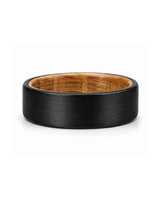 Black tungsten wedding ring with brushed finish and whiskey wood interior photographed lying flat on a white studio background.