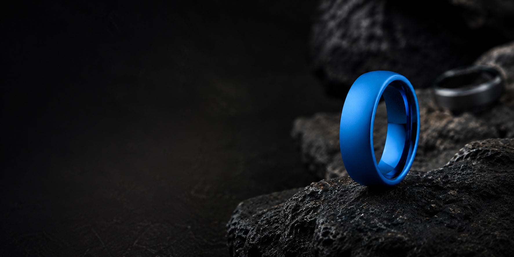 Luxury blue tungsten wedding ring hero banner with dark volcanic stone background and space for website text overlay