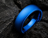 Ultra close-up macro photograph of a blue tungsten wedding ring showing detailed finish and texture against volcanic rock background