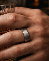 Close up of a man wearing a brushed silver tungsten wedding ring with a maple wood sleeve interior while holding a whiskey glass.