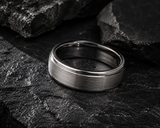 Close-up of a brushed silver tungsten wedding ring resting on dark slate stone with polished edges and rugged masculine styling