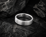 Close-up brushed silver tungsten wedding ring on dark slate stone with polished edges and rugged masculine styling