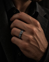 Close up of a man's hand wearing a polished black tungsten wedding ring with a rounded court profile against dark clothing.