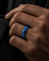 Close up of a man's hand wearing a polished blue tungsten wedding ring with a rounded court profile against dark clothing.