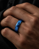 Close up of a man's hand wearing a polished blue tungsten wedding ring with a rounded court profile against dark clothing.
