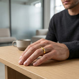 Man wearing a gold ring on a wooden table with a blurred background